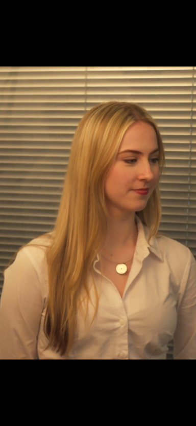 A woman with long blonde hair wearing a white shirt, looking to the side.