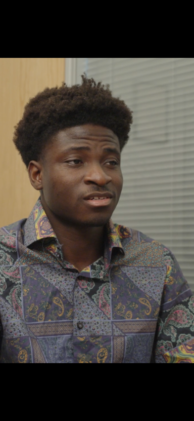 Young man wearing a patterned shirt, looking thoughtfully to the side.