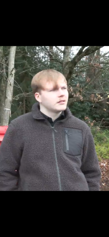 Young man with light brown hair wearing a dark jacket, standing outdoors.