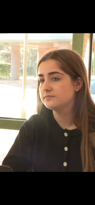 A young woman in a black top, looking thoughtfully out of a window.