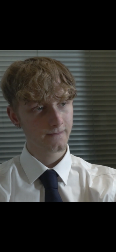 Young man with curly hair, wearing a white shirt and dark tie, appears thoughtful.