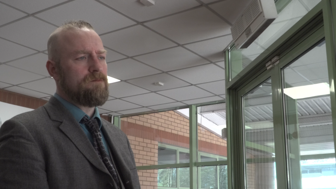Man in a suit stands in an office corridor, looking thoughtfully towards the window.