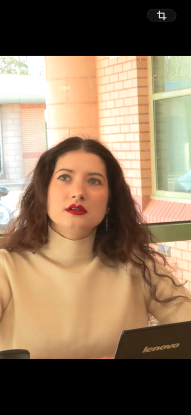 Young woman with long, curly hair, wearing a white turtleneck, looking thoughtfully upward.