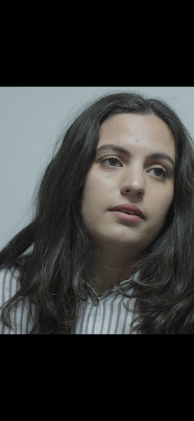 Young woman with long dark hair, wearing a striped shirt, looking thoughtfully.